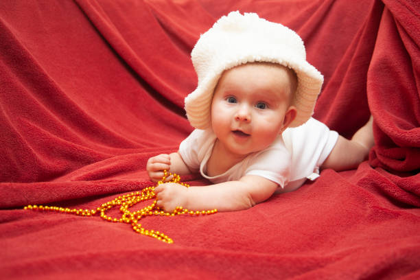 Infant baby on a red rug with Christmas and New Year's decorations.