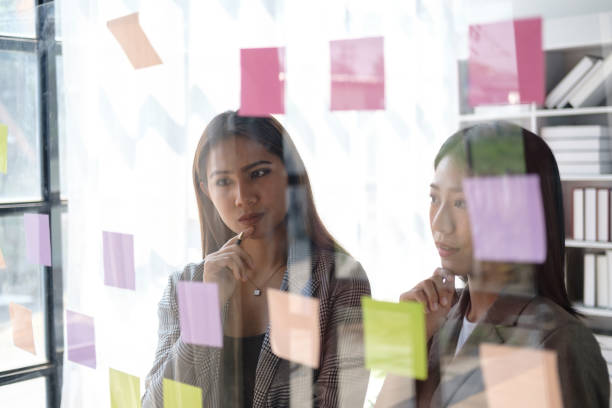 istock Young busineswoman with team brainstorming by use post it notes to share idea on glass wall. 1498454442