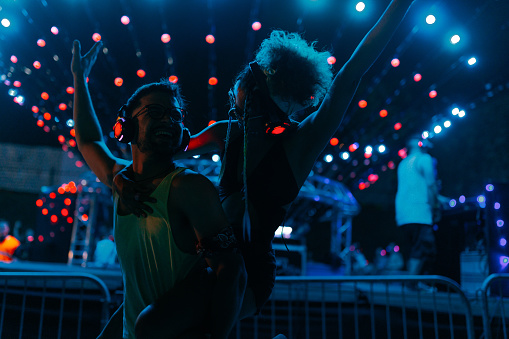 A young couple is dancing together as the boyfriend is holding his girlfriend in a piggy back ride. They are having headphones listening to the dj set at the festival.