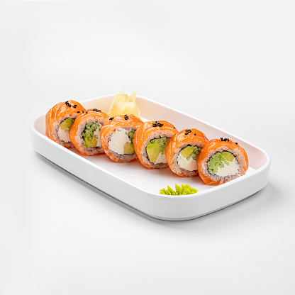 Set of sushi rolls with cream cheese, rice and salmon on a black board decorated with soy sauce and avocado on a dark wooden background. Japanese cuisine. Food photo background