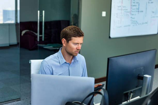 istock Confident young man businessman broker agent using mobile phone and pc computer working at desk in corporate office, serious. Concept of business development growth and solutions. Copy ad text space 1498456246