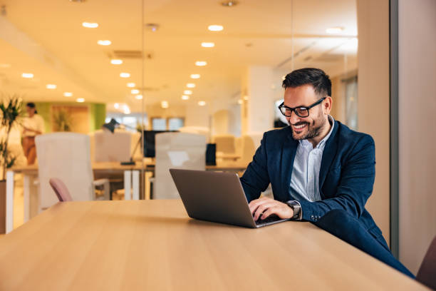 istock Smiling businessman chatting online with clients, using a laptop, sitting at the office. 1498460411