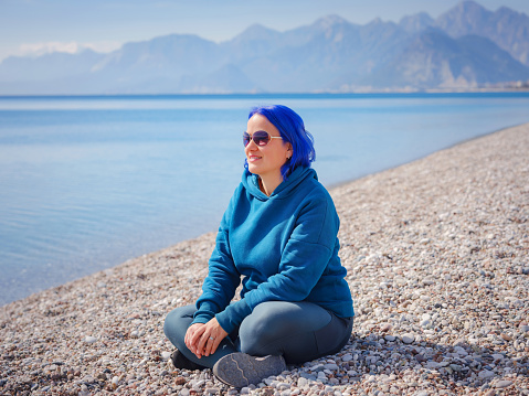 Female wearing light blue oversize hoodie and jeans. Blue haired woman outdoor at park near beach Antalya. Clothing mockup, Empty space for text o design.