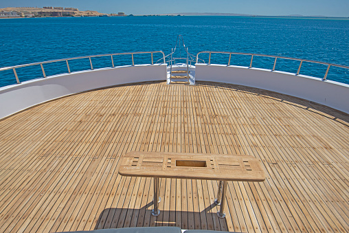 Teak bow deck of a large luxury motor yacht with wooden table and tropical sea view background