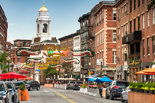 Boston, Massachusetts, USA – July 19, 2022:  People walk along Hanover Street by patio restaurants and shops and the city's oldest buildings along the Freedom Trail in the historic North End Little Italy neighbourhood of downtown Boston Massachusetts USA