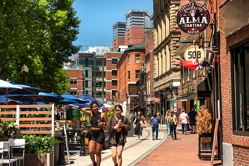 Boston, Massachusetts, USA – July 19, 2022:  People walk along Hanover Street by patio restaurants and shops and the city's oldest buildings along the Freedom Trail in the historic North End Little Italy neighbourhood of downtown Boston Massachusetts USA