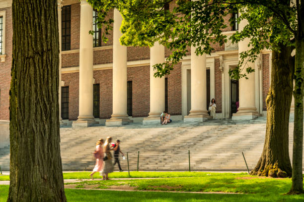 Boston, Massachusetts, USA – July 20, 2022:  Students walk by the stone steps of the grand library in Harvard Yard university campus in downtown Cambridge Massachusetts USA