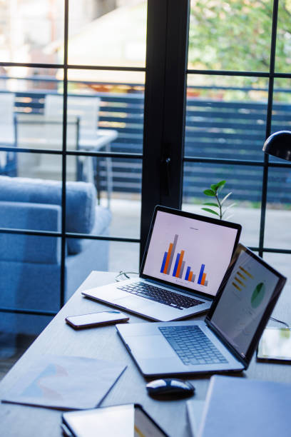 istock Desk by the window with two laptops with open graphs and pie charts regarding a project 1498468517