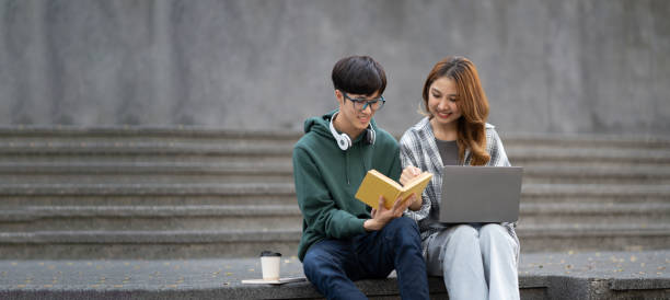 istock Young Asian college students reading books, studying on laptop, preparing for exam or working on group project while sitting on staircase of college campus. 1498470237