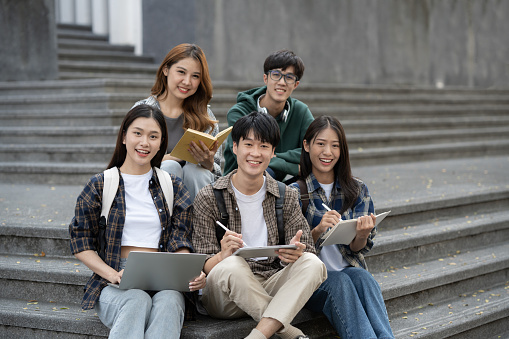 Potrait of young Asian college students working on group project while sitting on staircase of college campus.