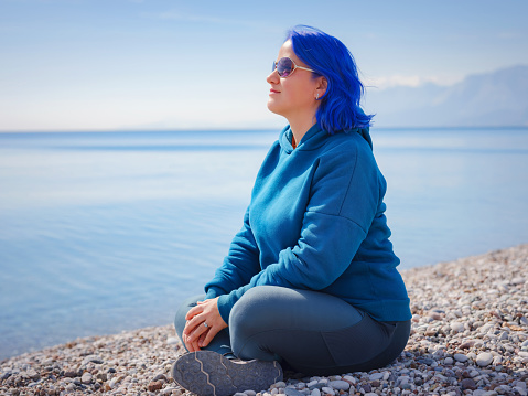 Female wearing light blue oversize hoodie and jeans. Blue haired woman outdoor at park near beach Antalya. Clothing mockup, Empty space for text o design.