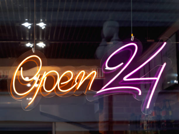 Glowing ad is OPEN 24 hours a day in cafeteria window. Modern electric signboard to attract attention of passers-by. Dark interior and colorful illuminated sign.