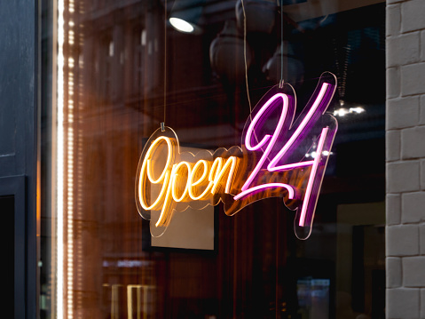 Glowing ad is OPEN 24 hours a day in cafeteria window. Modern electric signboard to attract attention of passers-by. Dark interior and colorful illuminated sign.