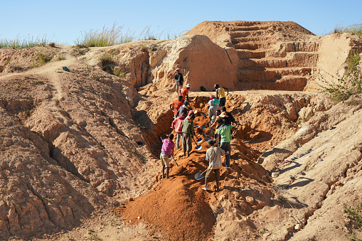 Ilakaka, Madagascar - April 30, 2019: Group of unknown Malagasy men mining sapphire in surface mine, by moving ground with shovels on a sunny day. This \