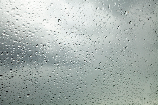 Raindrops on glass surface. Full frame view with cloudy sky background. Galicia, Spain.