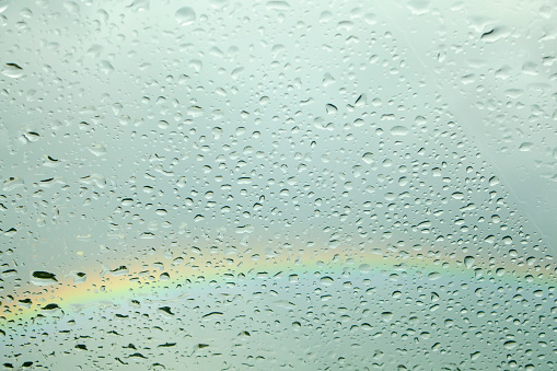 Raindrops on glass surface. Full frame view with rainbow and cloudy sky background. Galicia, Spain.