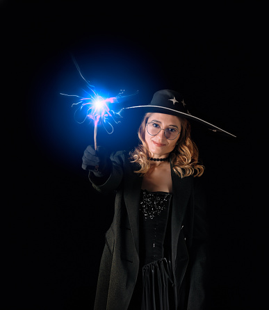 Woman with a magic wand in a hat and coat on black background