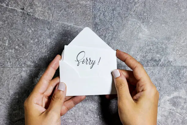 Photo of woman hand holding a white envelope with sorry concept on gray grunge background