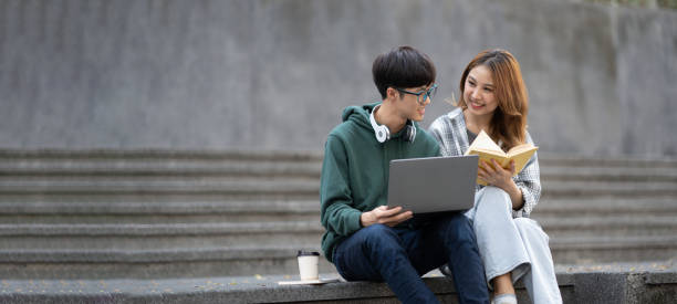 istock Young Asian college students reading books, studying on laptop, preparing for exam or working on group project while sitting on staircase of college campus. 1498481846