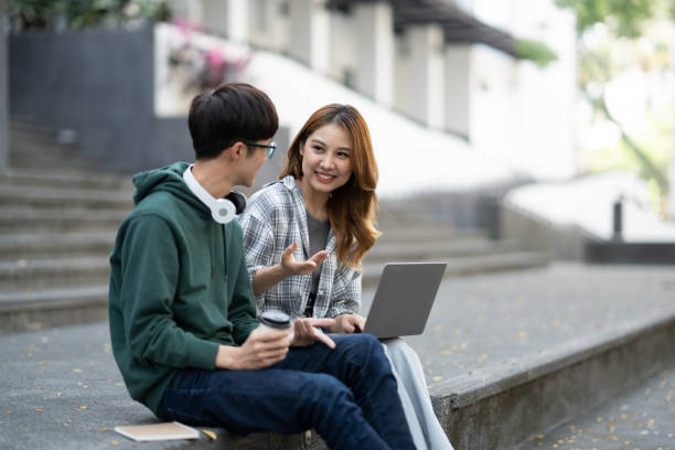 istock Young Asian college students reading books, studying on laptop, preparing for exam or working on group project while sitting on staircase of college campus. 1498482199