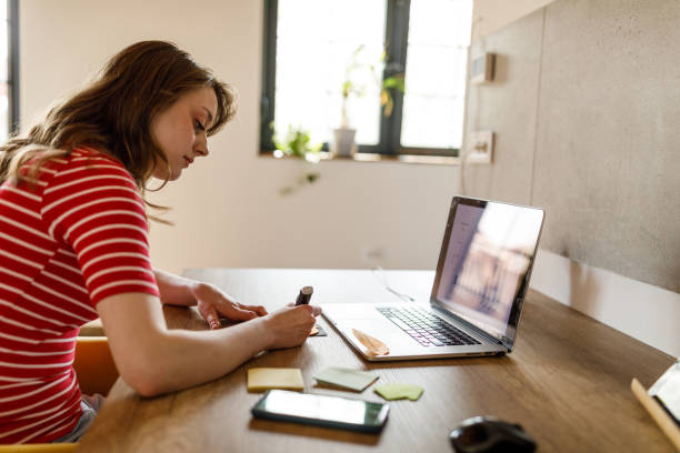 istock Young woman writing something on a sticky note at her desk 1498484673
