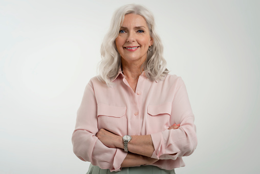 Studio portrait of grey haired senior woman looking at camera and smiling while standing at isolated white background. Copy space.