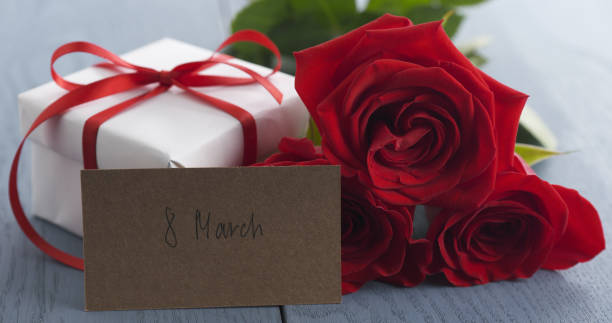 istock three red roses with gift box and paper card with 8 march phrase on blue wood table 1498487986