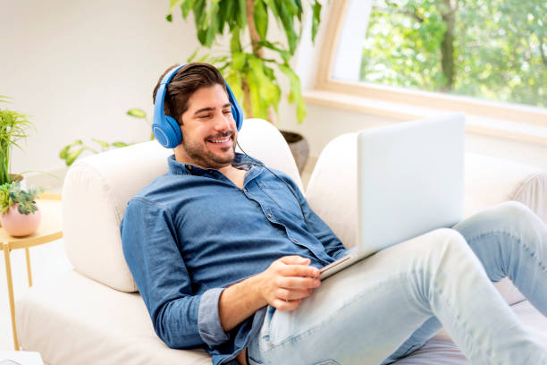 istock Confident man wearing headphone and using laptop while relaxing at home 1498488156