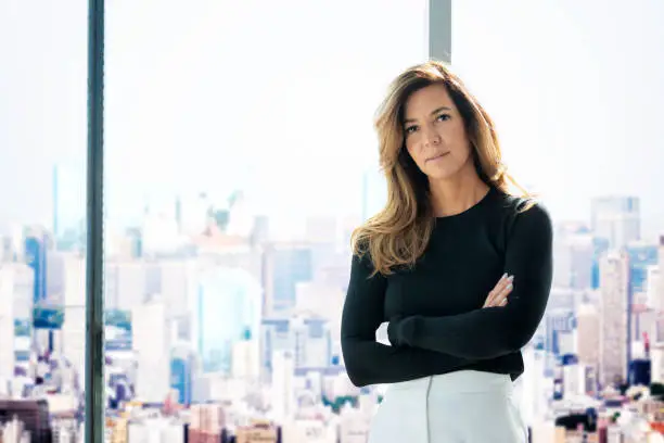 Portrait of an attractive businesswoman wearing sweater and trousers while standing at window and looking at camera.