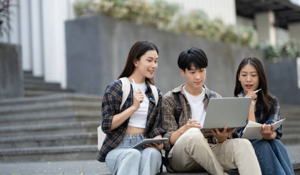 istock Young Asian college students reading books, studying on laptop, preparing for exam or working on group project while sitting on staircase of college campus. 1498491688