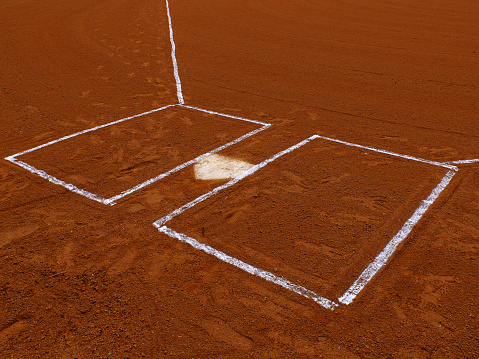 A low angle view of a new baseball sitting on the white baseline of a baseball diamond