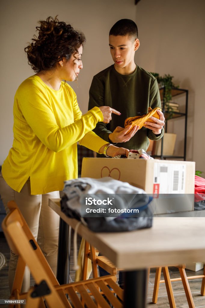 Teenage boy and his mother sorting out clothes that he's outgrown Candid shot of mid adult woman and her teenage son standing over a table, folding and sorting out various clothes that the boy has outgrown and putting it in a pile for donation. Pointing Stock Photo