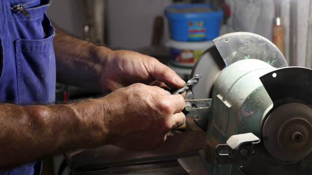 Man worker sharpens a drill at the grinder