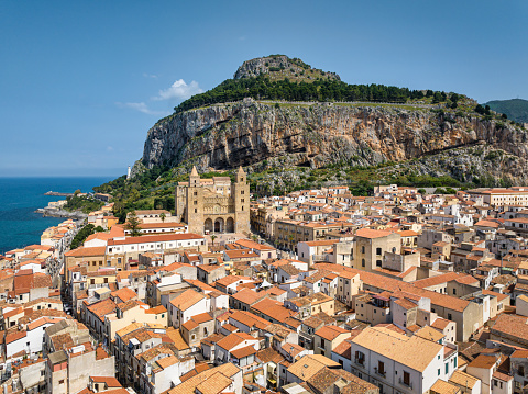 Cefalù City Aerial Drone Point of View over the coastal village at the mediterranean sea of the tyrrhenian coast. Famous Cefalù Cathedral in the village center and iconic hill La Rocca in the background of the Cefalu Old Town. Cefalu, Tyrrhenian Coast, Gibilmanna, Northern Sicily, Sicily Island, Italy, Southern Europe.