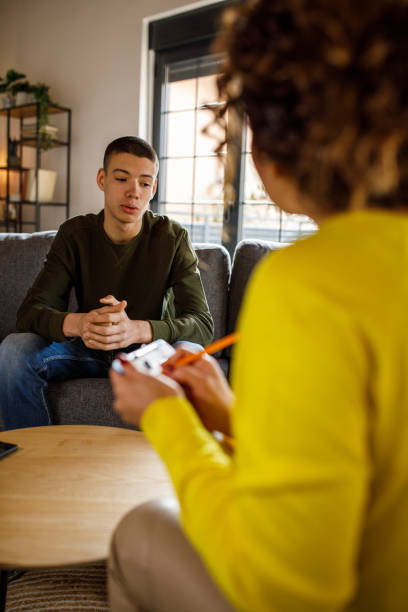 Caring female therapist talking with insecure teenage boy stock photo