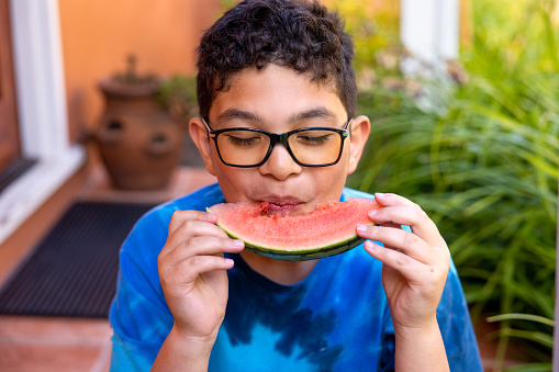 High quality stock photo of an mixed race boy eating watermelon on the porch during a summer time party.
