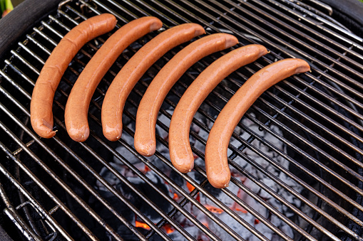 High quality stock photo of an grilled hotdogs cooking over open coasl for a summer time party at home in the backyard.