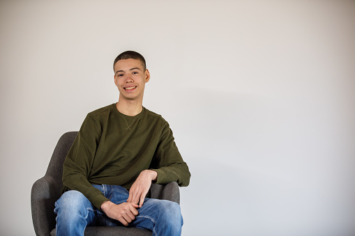 Copy space shot of charming teenage boy sitting in a chair against a white background, smiling.