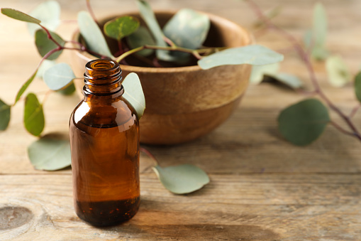Bottle of eucalyptus essential oil and leaves on wooden table. Space for text