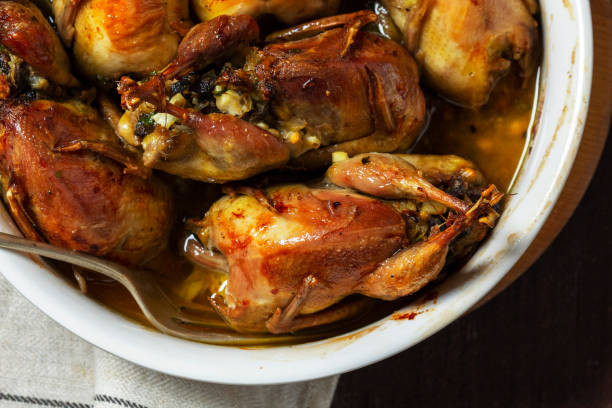 Baked quail stuffed with mushrooms, eggs and bread in a ceramic form on a wooden table.