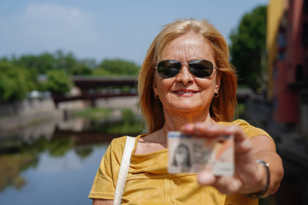 mulher imigrante idosa orgulhosa e sorridente mostrando seu documento de identidade (documento de identidade nacional espanhol) do lado de fora. uma senhora com seu documento de identidade - immigrant women sunglasses portrait - fotografias e filmes do acervo
