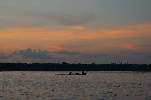 Golden sunset on calm Amazon river. Boat with unrecognizable fishermen