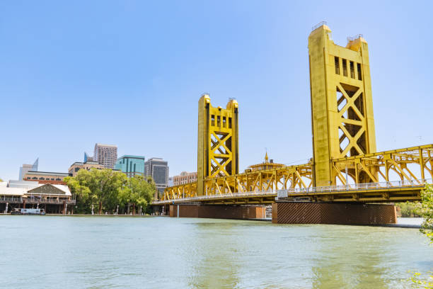 Aerial view of Sacramento, California, featuring the golden Tower Bridge over the Sacramento River, city skyline, and State Capitol Building under a clear sky.
