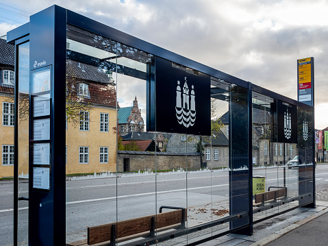 Copenhagen, Denmark - Oct 23, 2018: Modern suburban public bus stop constructed mainly using glass panels. Relaxing late afternoon city urban scene. European style buildings around.