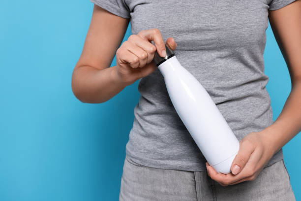 istock Woman holding thermo bottle on light blue background, closeup. Space for text 1498504508