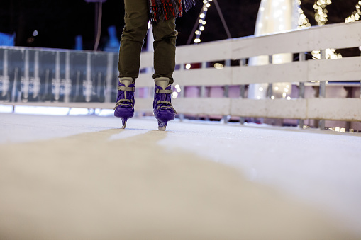 Low section of unrecognizable young man wearing blue ice skates and ice skating at the ice rink on a cold winter's evening.