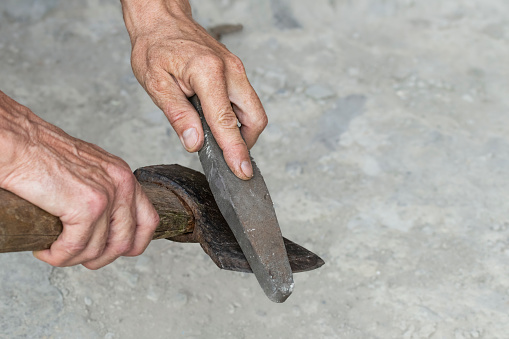 Sharpening the blade of an axe. A man sharpens the blade of an old rusty axe by hand with a grindstone.