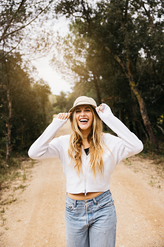 Portrait of young beautiful blonde woman wearing a hat happily walking on a path in a forest