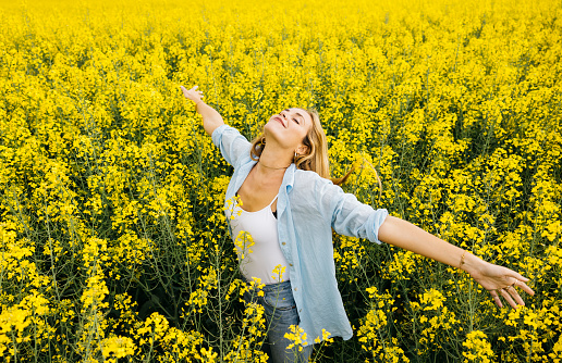 Beautiful young blonde cheerful woman, with outstretched arms, amidst a field of blooming yellow rapeseed flowers