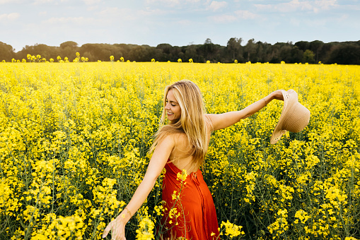 Beautiful young blonde cheerful woman, with outstretched arms, amidst a field of blooming yellow rapeseed flowers